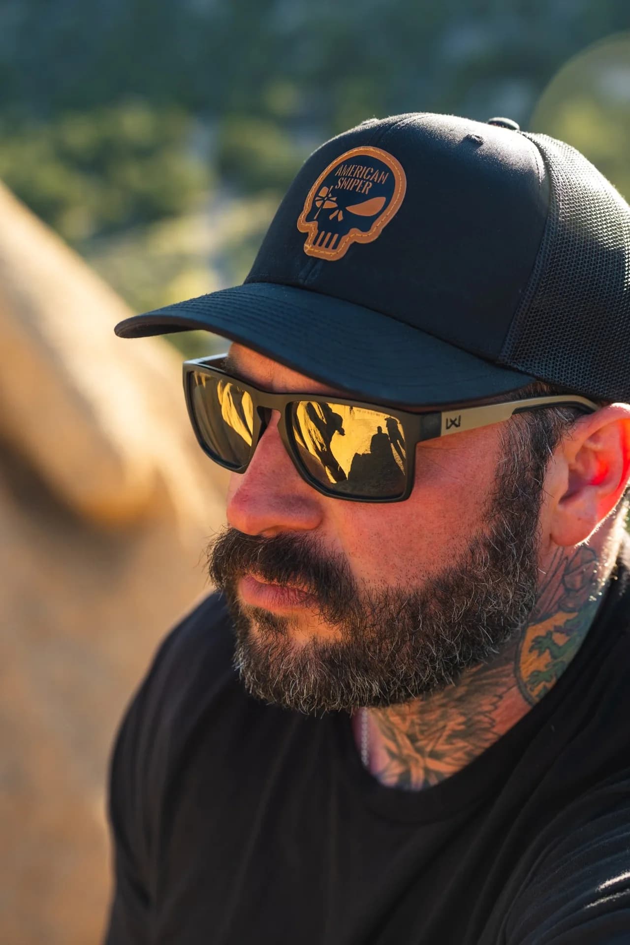 A man wearing an American Sniper cap and sunglasses in golden evening light.